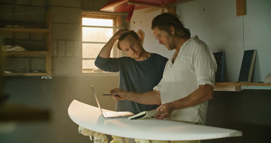 Man in surfboard related office describes items to customer who smiles