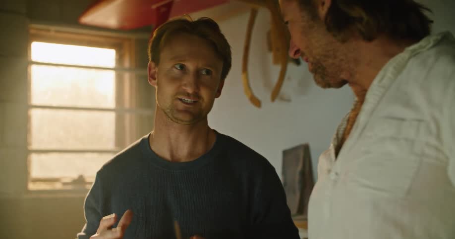 Two man excitedly discussing the design of a surfboard inside a workshop