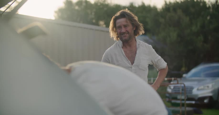 A man hands another man a surfboard to load in the back of his vehicle