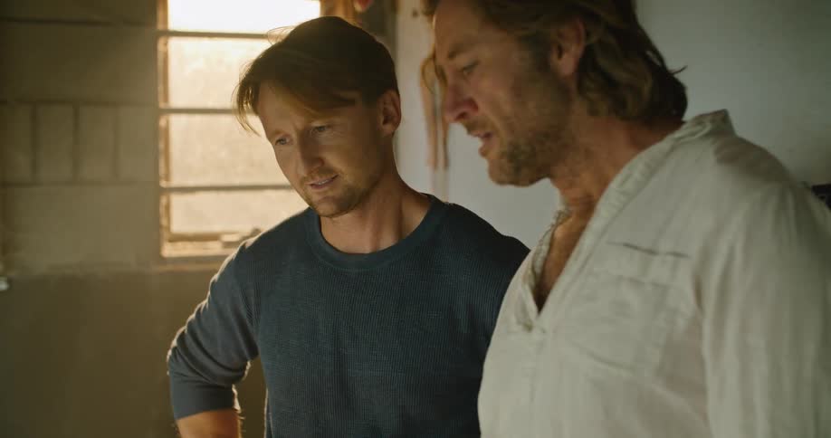 Two men are talking together indoors at dusk