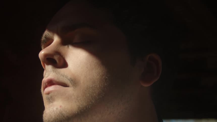 A man in a room with eyes close with the sun shining on his face