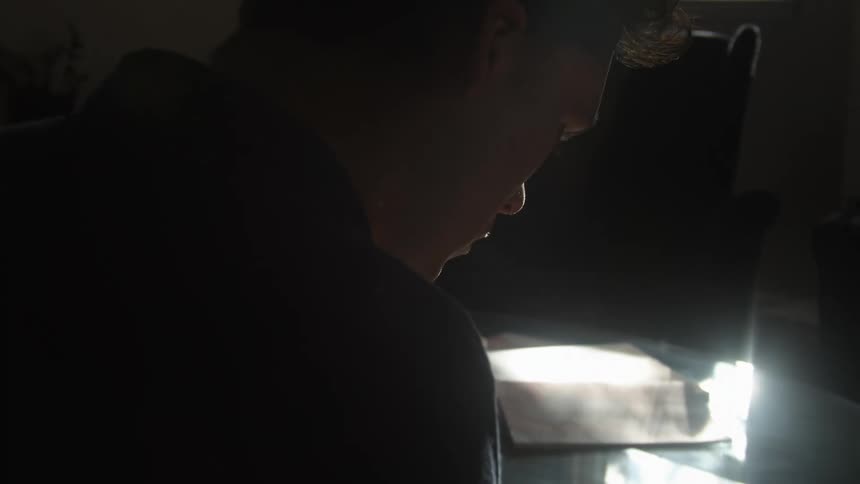 Silhouette of a young man playing a drum inside a dimly lit room