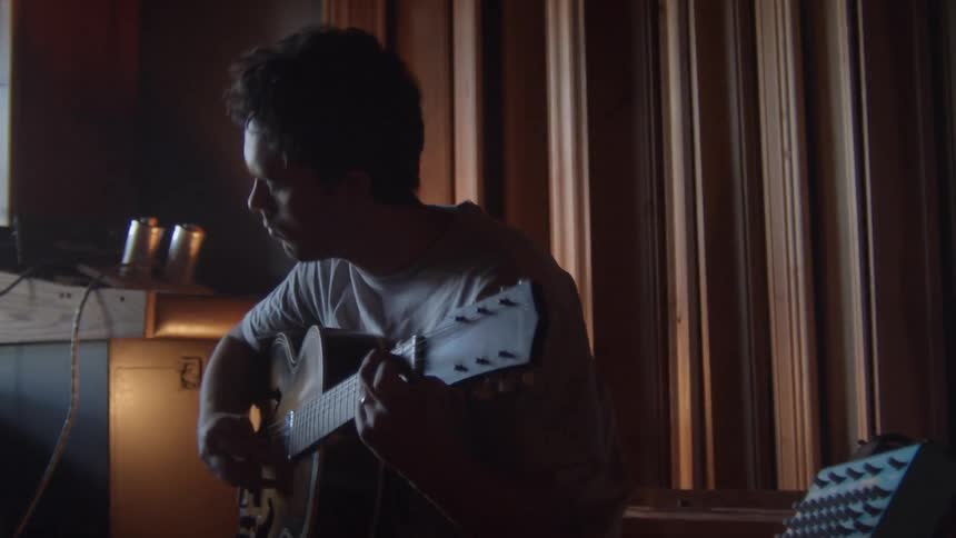 Man with a white t shirt playing the guitar is silhouetted in the studio
