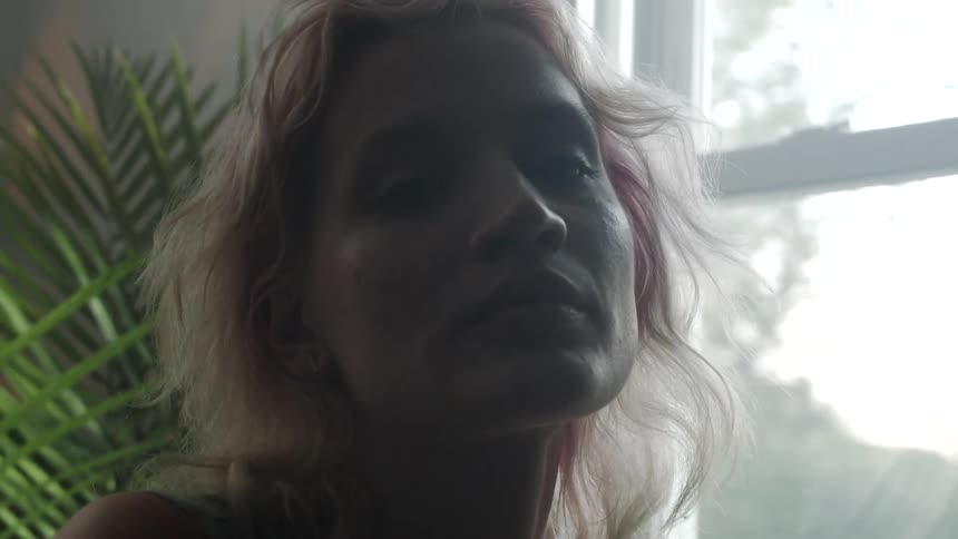 Blonde woman looks at the camera next to the window