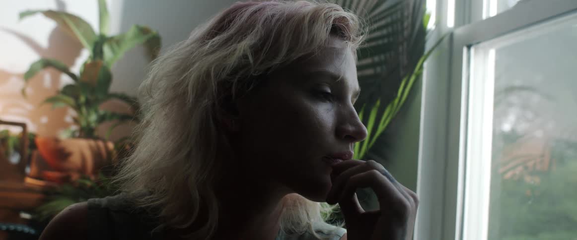 Blonde woman pensively touches her lips inside a dimly lit room