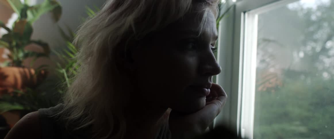 Side view of blonde woman standing next to the window is silhouetted