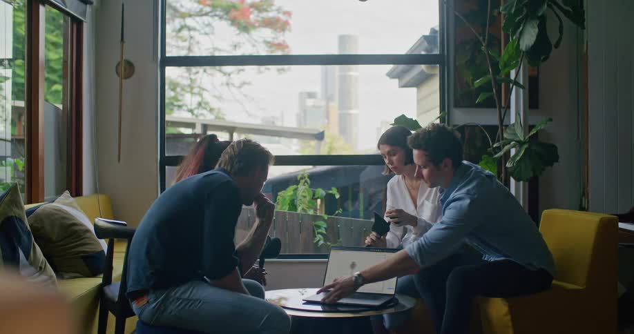 Man moves a laptop on a table while sitting with another man and two women