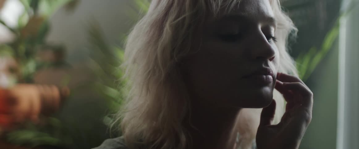 Blonde woman rests her head on her hand while sitting in a dimly lit room