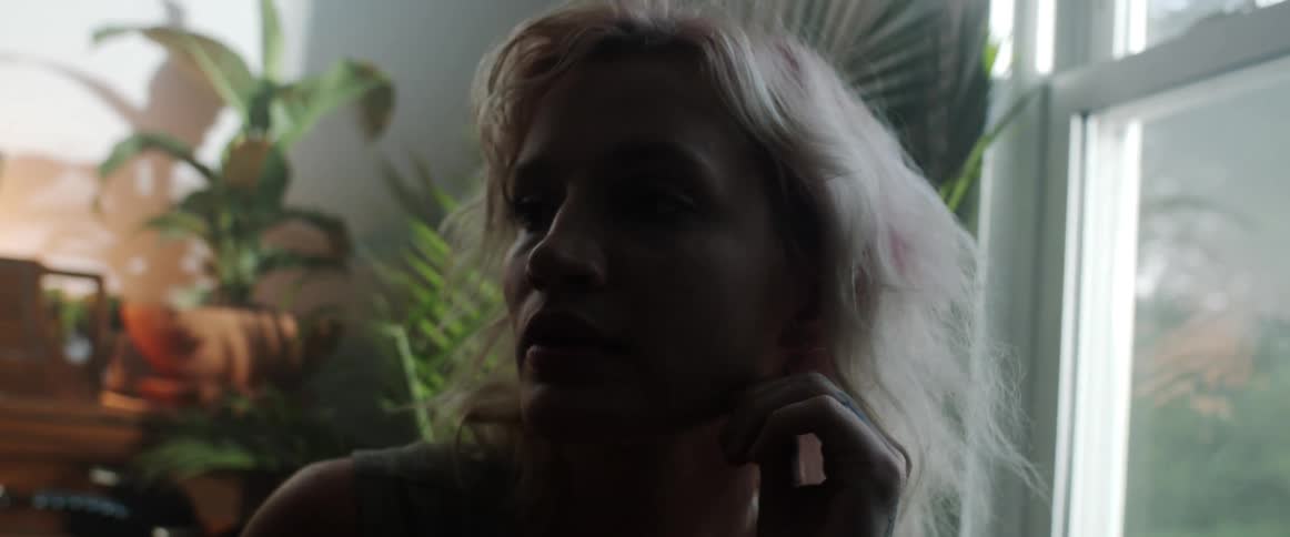 A woman in a room with plants a wall and a window in the background