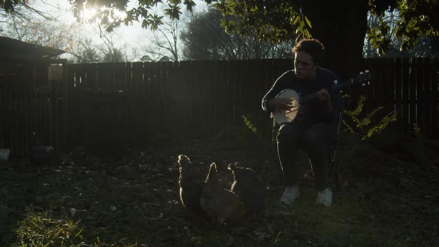 A man playing banjo outdoors to chickens