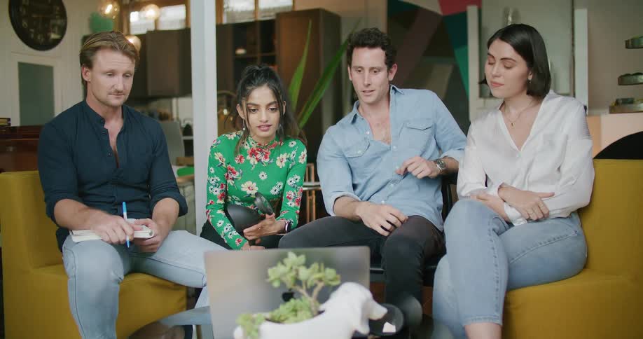 Two men and two women sitting on couches and chairs in a room and looking at a laptop