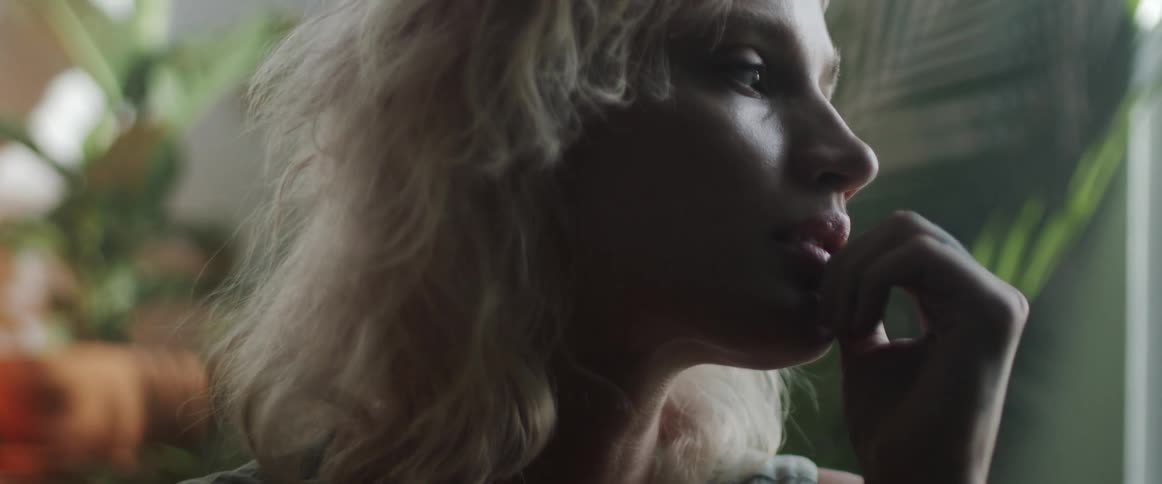 Blonde woman pensively touches her lips inside a dimly lit room