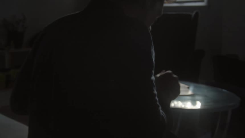 Silhouette of a young man playing drums inside a dimly lit room