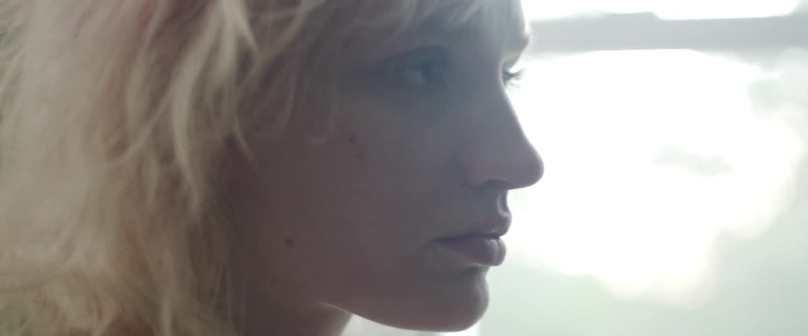 A woman in a room with a plant a wall and a window in the background