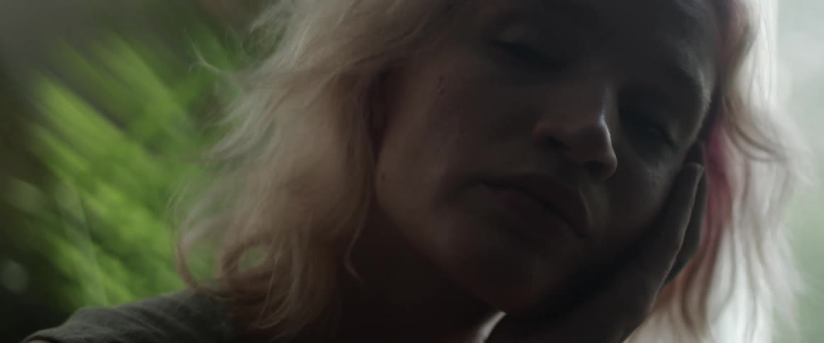 Blonde woman pensively touches her face inside a dimly lit room