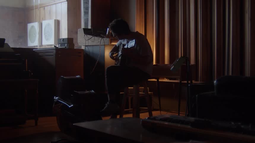 Man sitting on a stool plays guitar in the studio