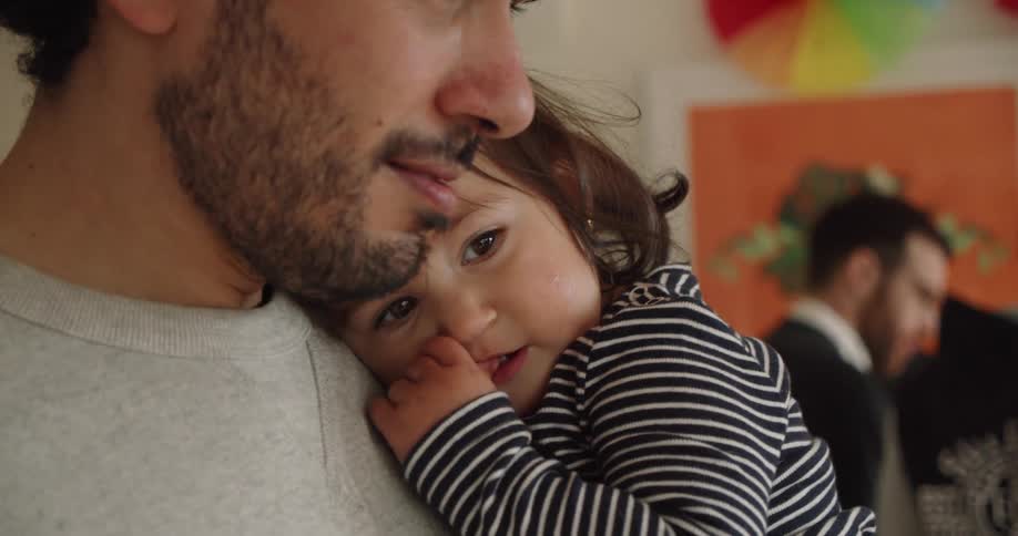 A young girl laughs and hugs her father while he holds her at a party