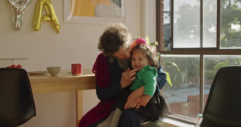 Girl in a green dress sitting in the lap of her mother at home