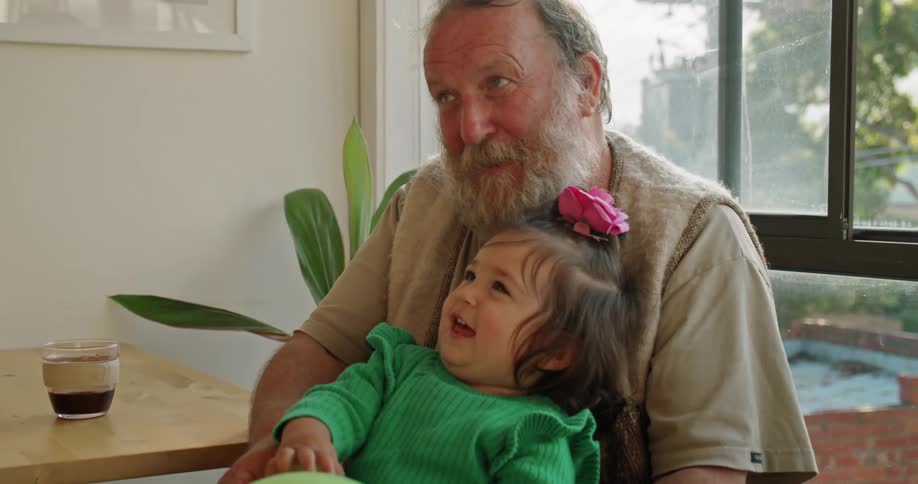 An older man holds a baby with a balloon and another man tickles the baby to laugh