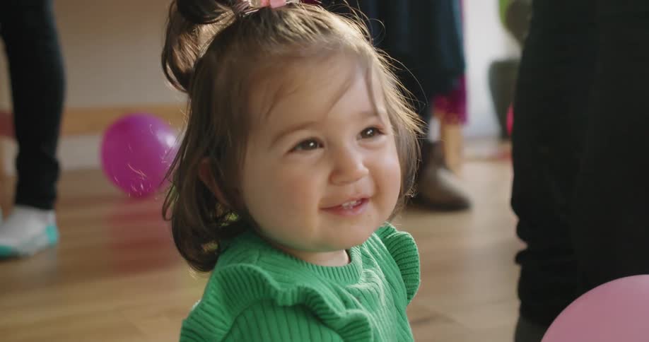 Little girl wearing a green dress sitting on the floor of a room in a birthday party