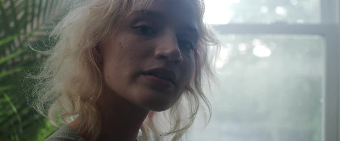 Blonde woman faces the camera with eye contact next to the window