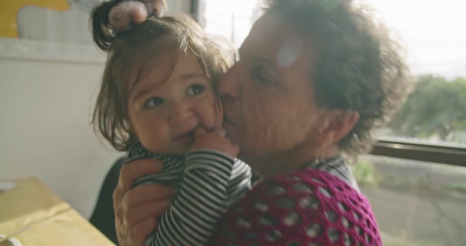 Grandmother hugging and kissing her granddaughter at home