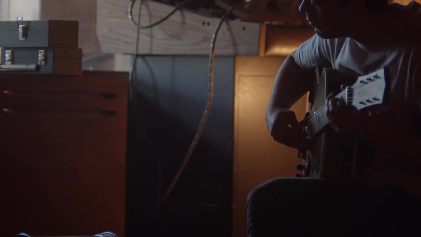 Man with a white t shirt playing guitar is silhouetted in the studio