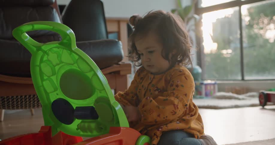 A baby girl sits on the floor playing with a push style toy