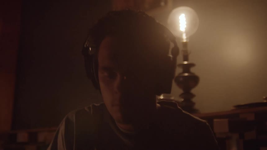 Male drummer with headphones plays drum in a dimly lit room