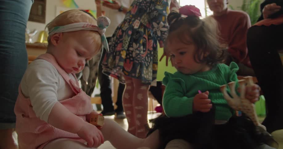 Mothers at party watch kids play together as others stand around eating