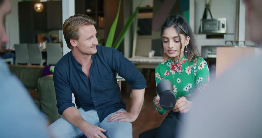 A man and a woman sitting inside of a room talking and looking over a black lamp