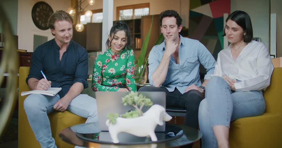Office workers wearing casual clothes sit on couch video conferencing on laptop as one of them is ready to take notes