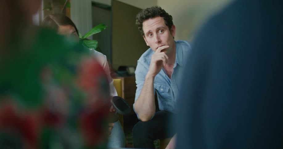 A man and a woman sitting on chairs in a room with a wall and a door in the background