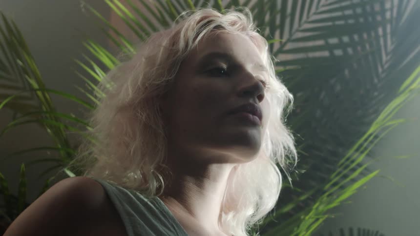 A woman relaxing near a large house plant looks into the camera before turning away