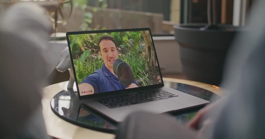 Workers in office video call with coworker outdoors showing them object with garden in background