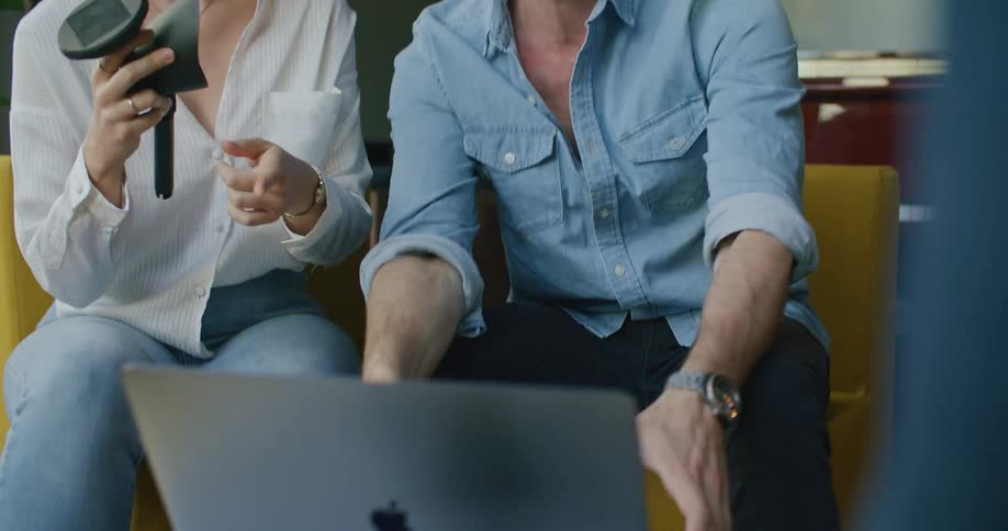 A man and a woman sitting on couches looking at a laptop with a wall and door in the background
