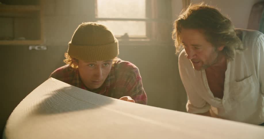 Boss teaching an apprentice to work on a surfboard in the workshop
