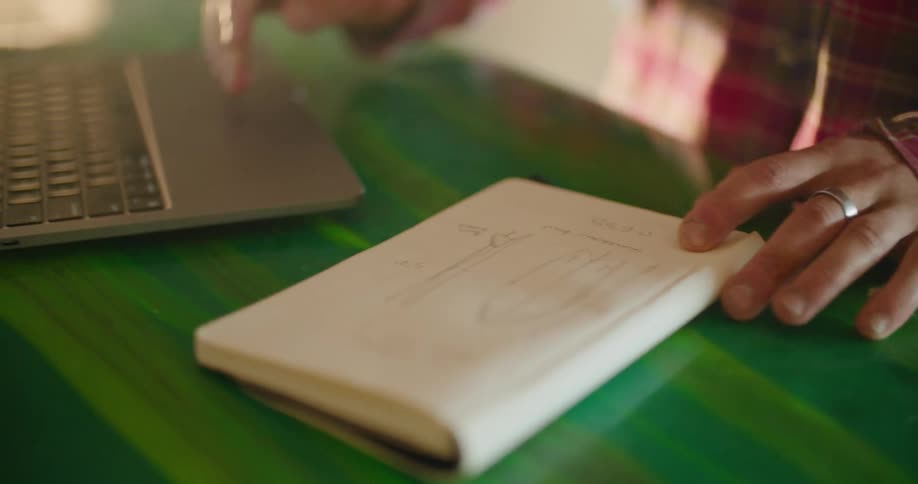 A person with a pencil and pad sitting at a desk and using a laptop