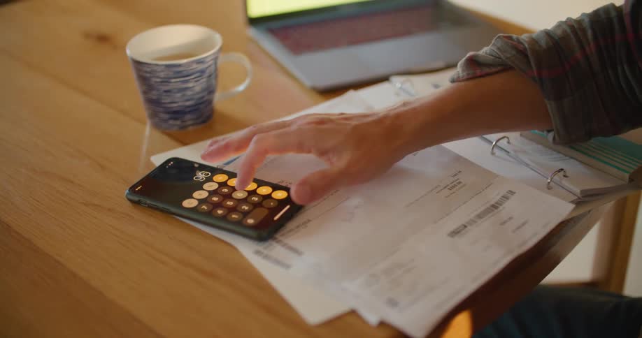 A man uses the calculator app on his smartphone while paying bills