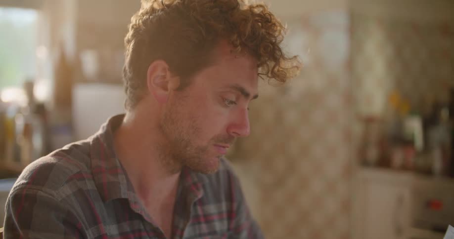 A man is sitting at the kitchen table looking at a bill
