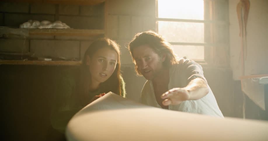 A man and girl measure a surfboard together