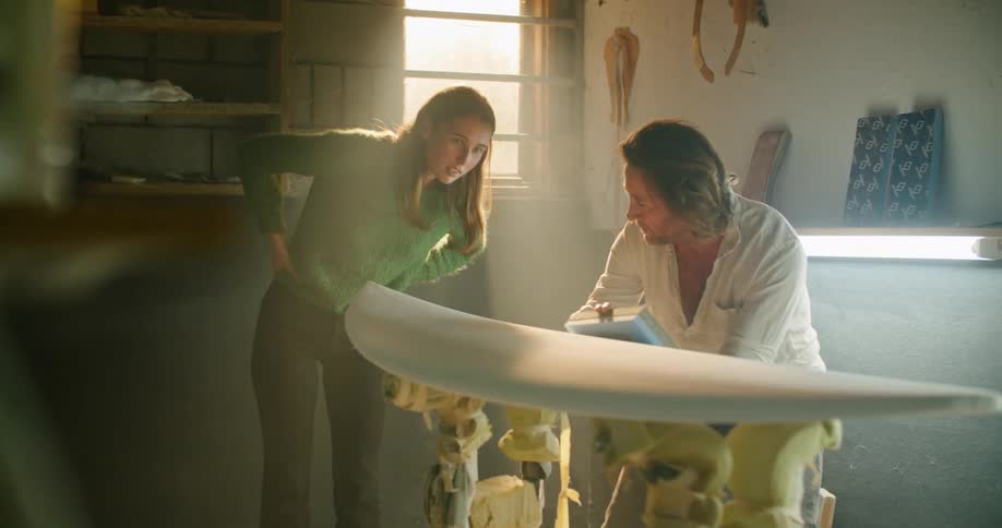 Older man demonstrates sanding surfboard to woman
