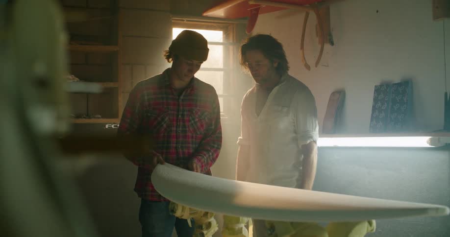 Two men examine a surfboard they are making
