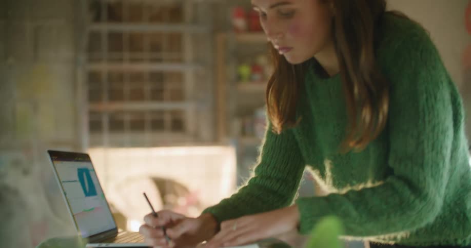 A woman is standing indoors and working on a laptop