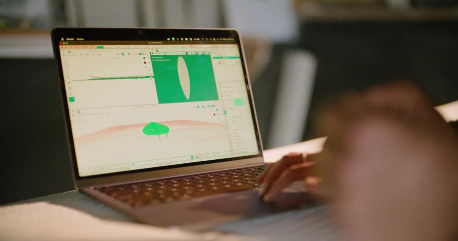 A person designing a surfboard on a laptop inside a workshop