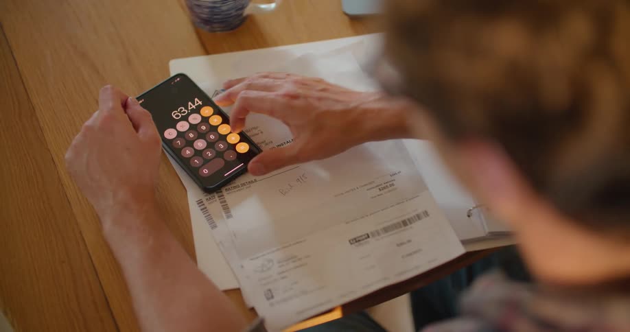 A person is adding up bills on a calculator