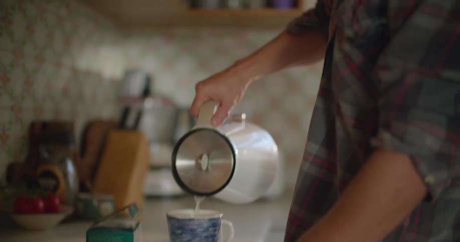 A man with glasses pouring hot water from a kettle into a mug