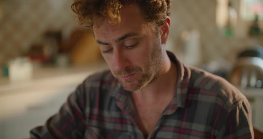 A man is drinking coffee and sitting at a table in his kitchen