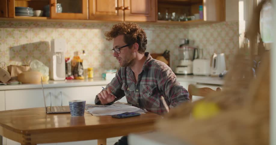A man is talking on his phone at the kitchen table