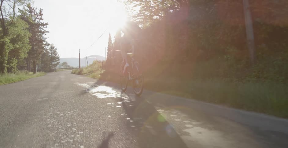 A bicyclist rides on a country road into bright sunshine